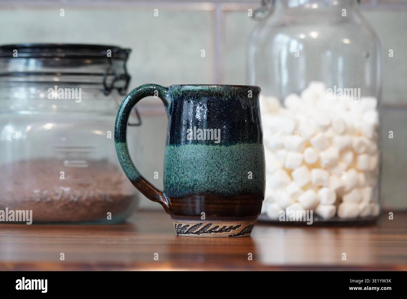 Tazza verde fatta a mano con cioccolato in polvere e marshmallow in contenitori di vetro sullo sfondo per preparare una gustosa bevanda calda al cioccolato Foto Stock