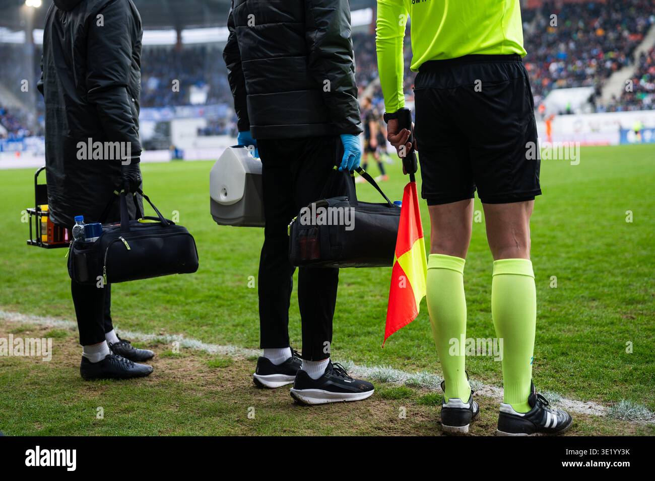 Assistente arbitro con una bandiera si trova accanto al personale medico con borse di emergenza a bordo campo durante una partita di calcio professionale. Foto Stock