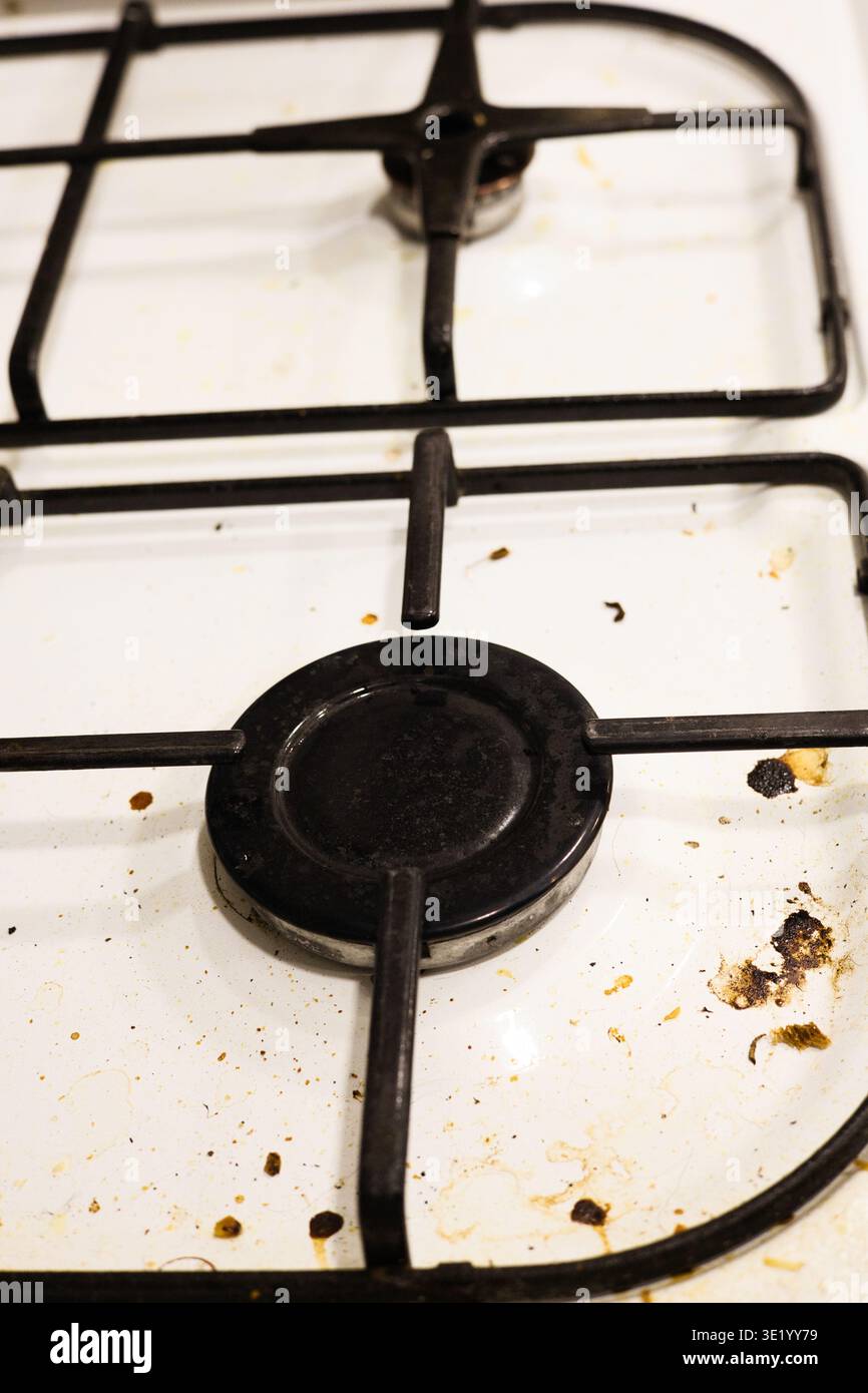 Un colpo top-down professionale di un piano cottura a gas bianco ricoperto da schizzi di grasso, particelle di cibo essiccate e macchie. L'immagine acquisisce lo stato di A. Foto Stock