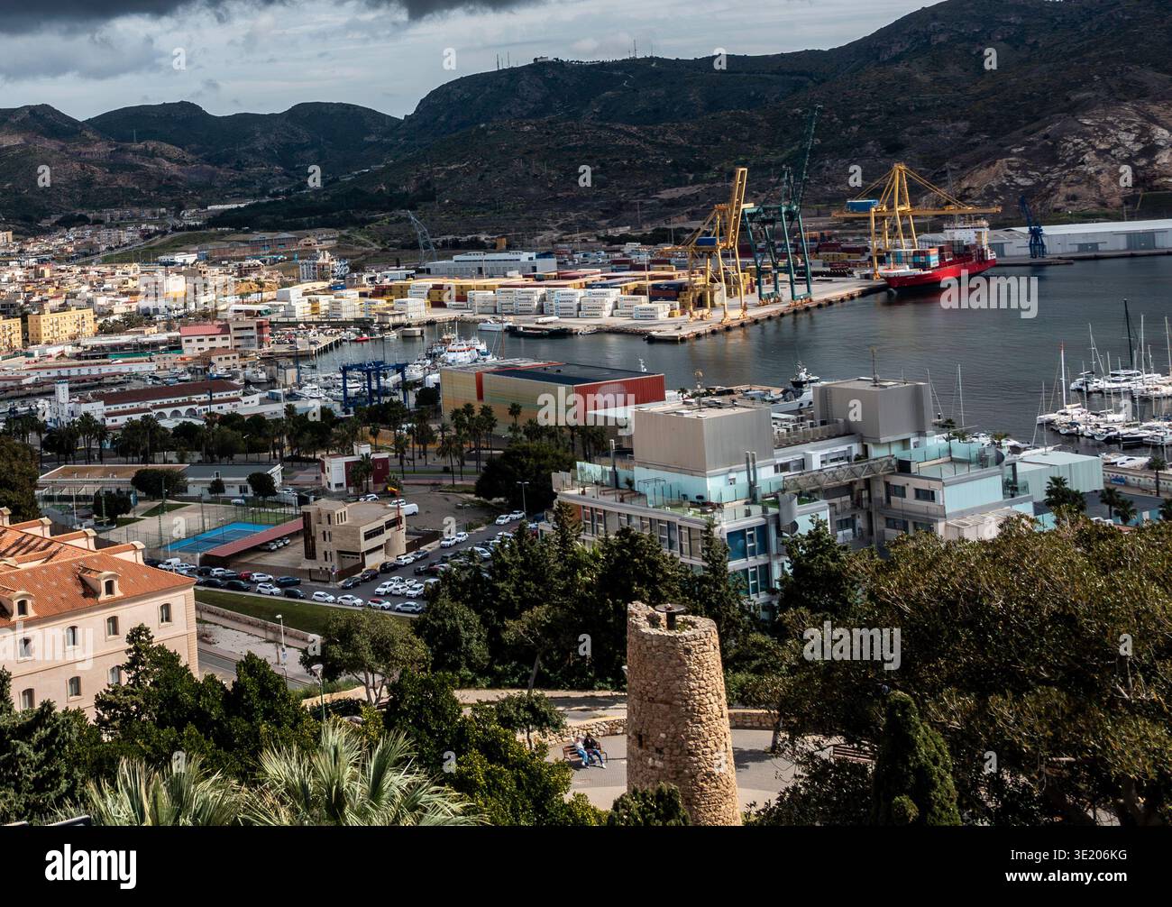 Una veduta sopraelevata del porto di Cartagena, Spagna, mostra container, gru, navi ormeggiate, e edifici urbani sullo sfondo di una montagna. Foto Stock