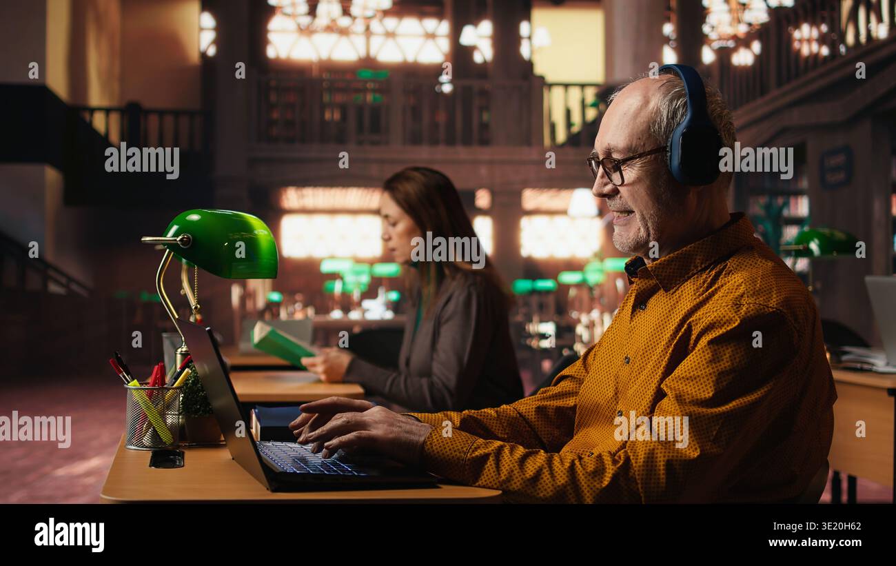 Adulto anziano che disturba le altre persone in biblioteca con il suo rumore musicale, ascoltando musica ad alto volume e cantando alla scrivania. Un uomo anziano che rompe le regole della biblioteca con canzoni solide. Foto Stock