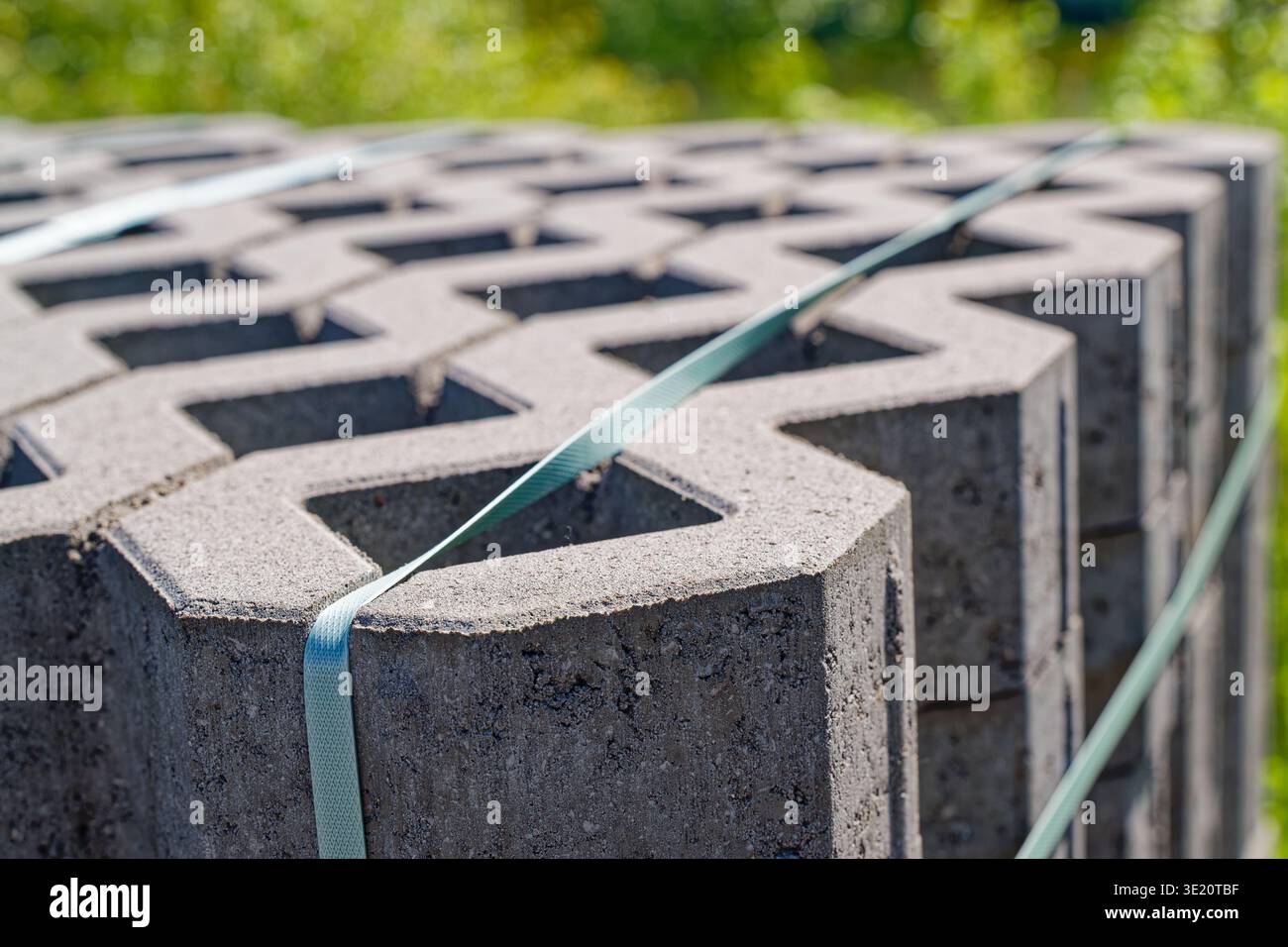 Un fascio di blocchi di calcestruzzo grigio con centri cavi strettamente legati con fasce verdi pronte per l'uso in esterni con dorso verde sfocato Foto Stock
