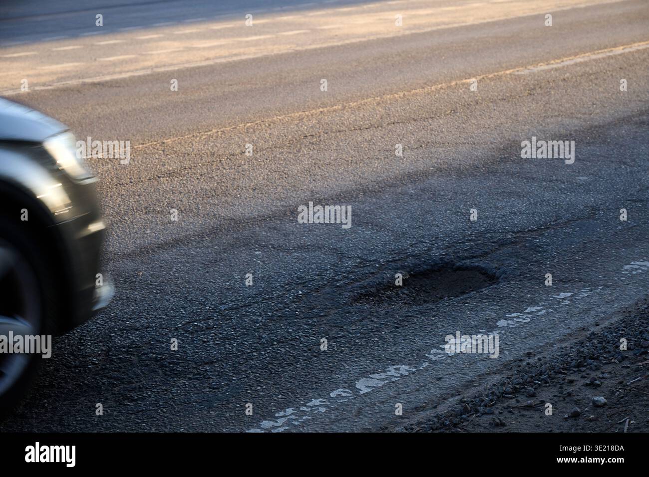 Uno scatto dinamico dall'angolazione ridotta e primo piano che cattura la parte anteriore di un'auto, con fari e ruote sfocati, passando davanti a una grossa buca Foto Stock