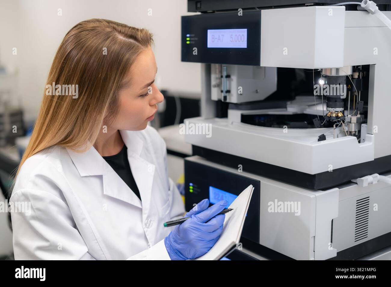 Tecnico di laboratorio che prende appunti durante l'utilizzo di una sofisticata macchina per cromatografia HPLC presso un centro di ricerca. Foto Stock