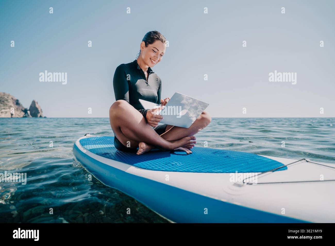 Donna Paddleboard Ocean Reading - Una donna siede su un paddleboard nell'oceano, a leggere un libro. Foto Stock