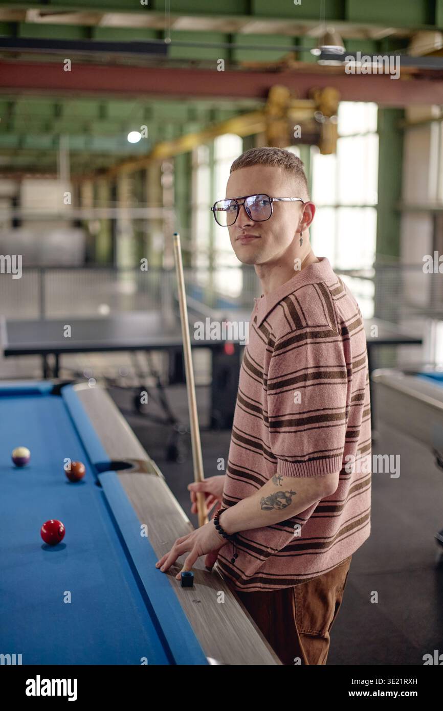 Ritratto verticale di un giovane adulto che gioca a biliardo in ambiente industriale Foto Stock