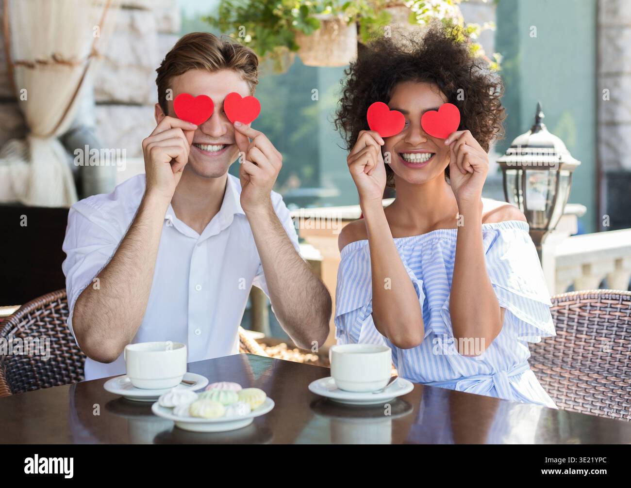 Felice coppia interrazziale con cuori di carta nel caffè Foto Stock
