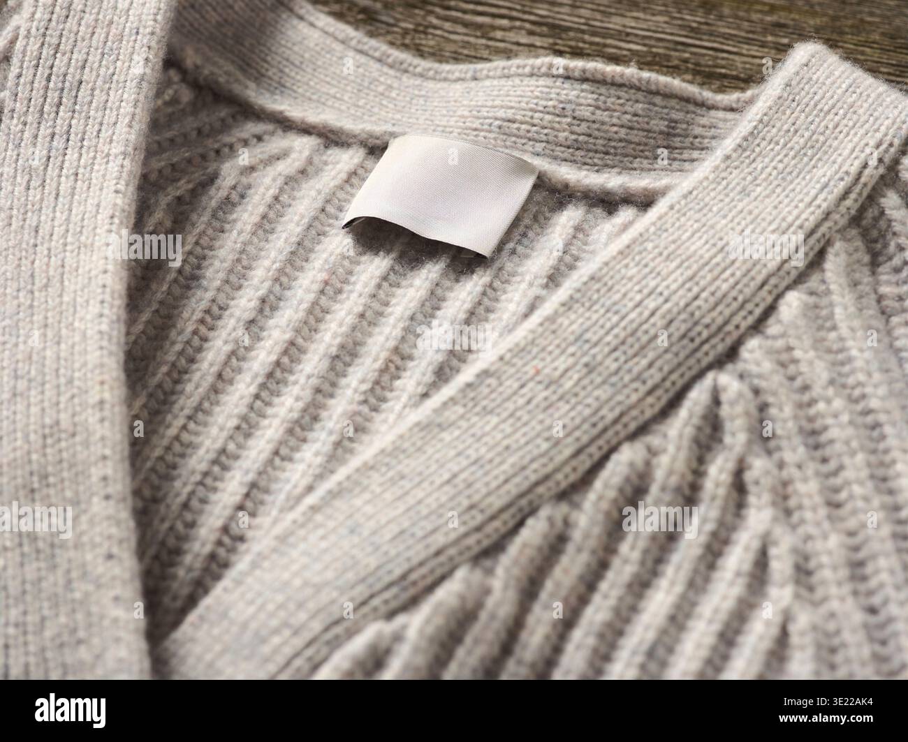 Primo piano di un maglione in maglia beige con un'etichetta vuota su sfondo in legno. Germania Foto Stock