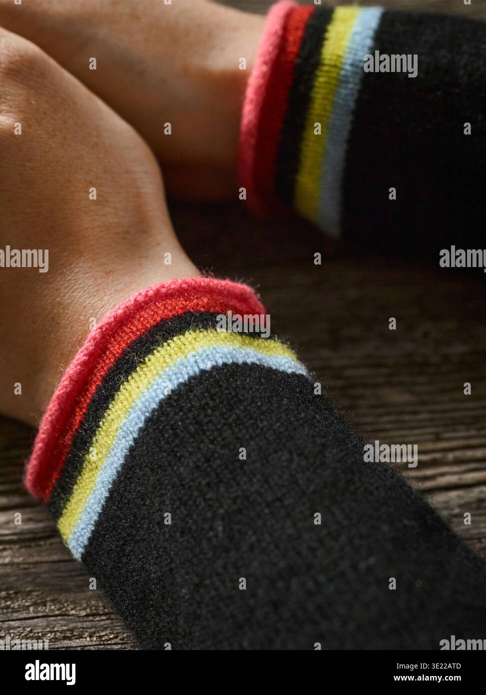 Mani appoggiate su una superficie in legno con maniche nere e polsini colorati a righe. Germania Foto Stock