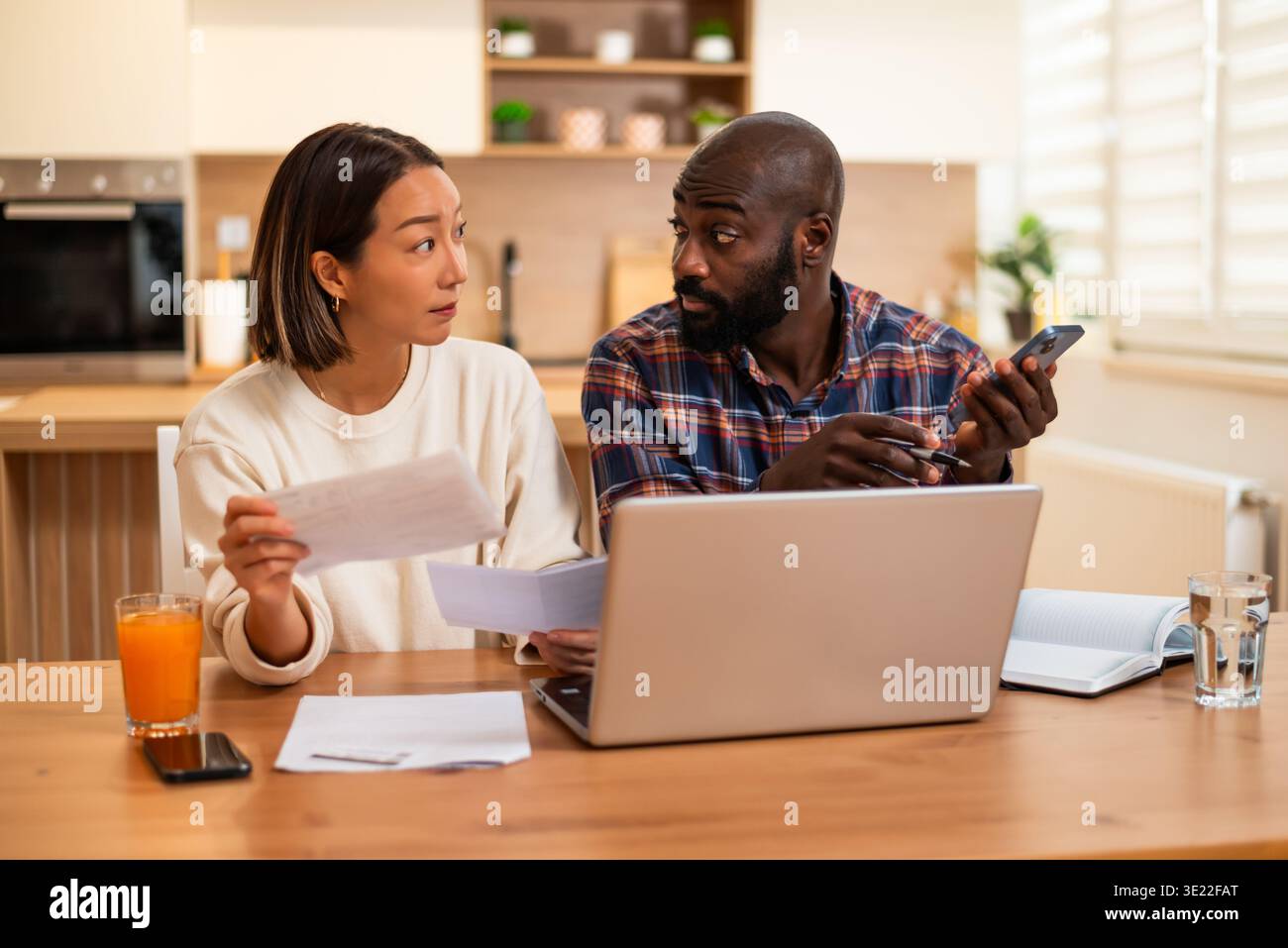 Le coppie multirazziali esaminano i documenti finanziari insieme a casa, apparendo concentrati e leggermente preoccupati mentre discutono le loro spese. Foto Stock