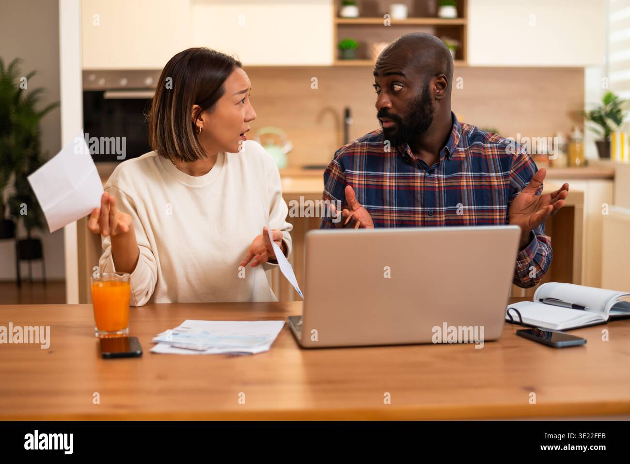 Le coppie multirazziali esaminano i documenti finanziari insieme a casa, apparendo concentrati e leggermente preoccupati mentre discutono le loro spese. Foto Stock