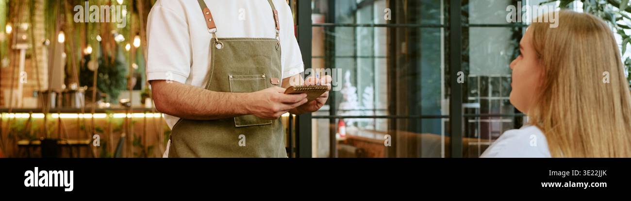Giovane donna che ordina cibo dal cameriere nel ristorante moderno Foto Stock