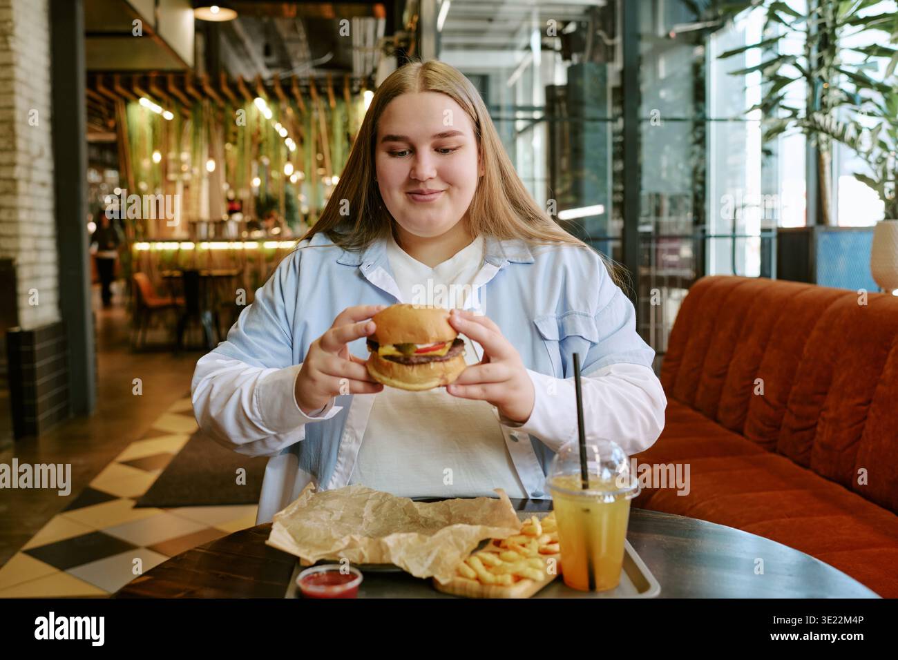 Giovane donna sorridente mentre tiene in mano un hamburger e siede al Cafe' Foto Stock