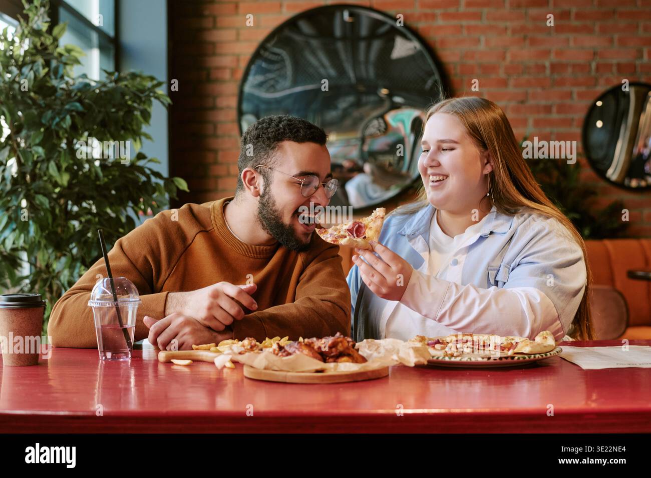 Giovane donna che dà da mangiare alla pizza giovane uomo mediorientale mentre sorride in casa Foto Stock
