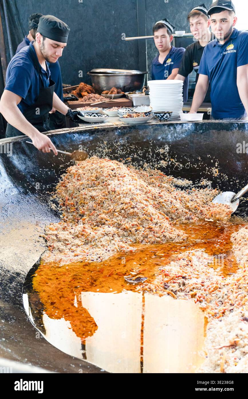 Tashkent (Toshkent), Uzbekistan (o'zbekiston) - 26 maggio 2025: Vista verticale degli chef serve plov tradizionale uzbeko da un enorme calderone in ghisa a. Foto Stock
