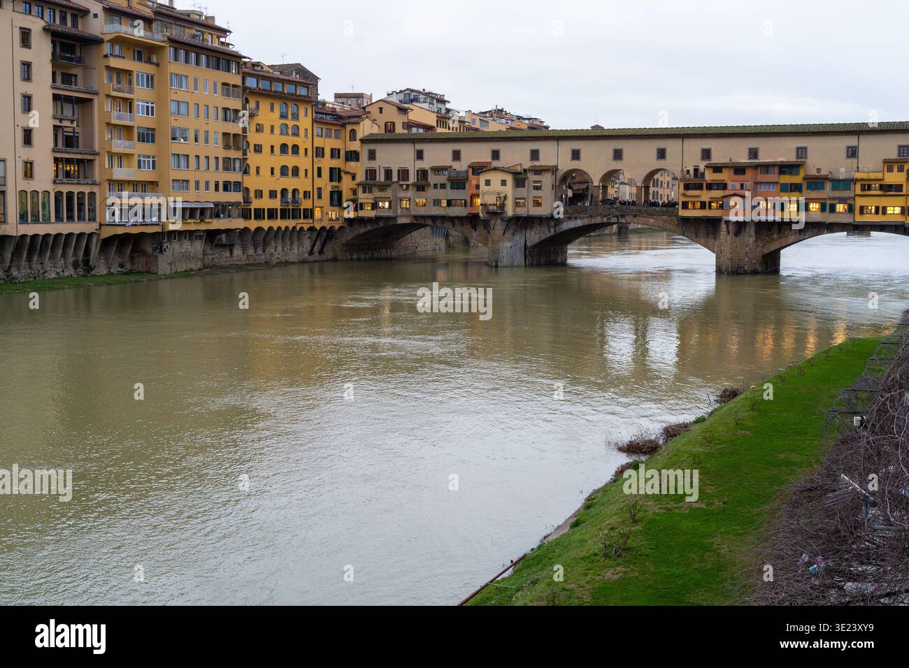 Lo storico Ponte Vecchio, fiancheggiato da negozi, attraversa il fiume Arno sotto un cielo nuvoloso a Firenze Foto Stock