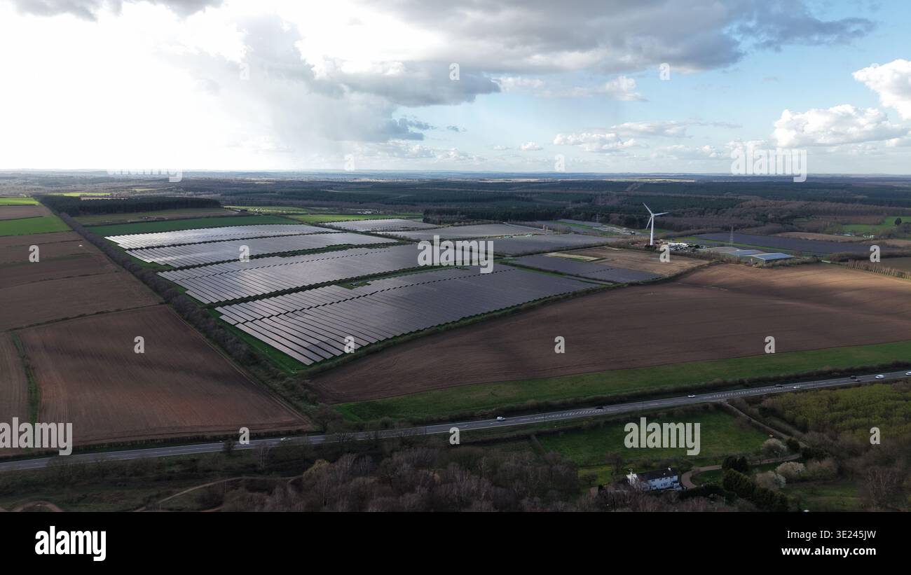 Vista aerea di ampi pannelli solari che brillano sotto un cielo opaco lungo campi verdeggianti e boschi scuri, Kirklington Road, Newark, Regno Unito. Foto Stock