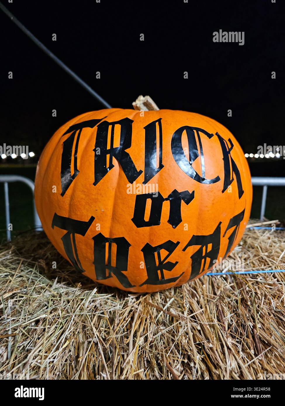 Una zucca siede su una balla di fieno con "Trick or Treat" dipinto di nero, catturando lo spirito divertente e spettrale di Halloween. Foto Stock