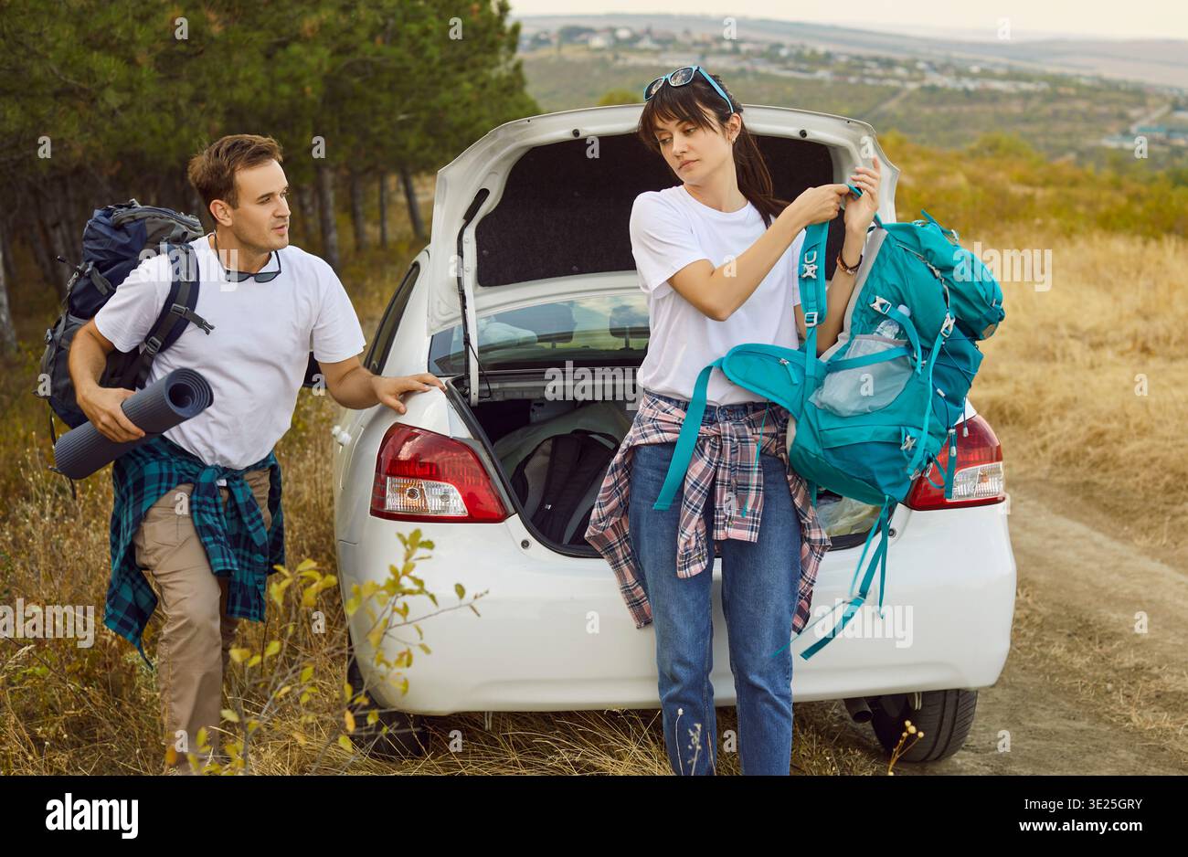 Coppia con zaini che scaricano il bagagliaio dell'auto prima di fare un'escursione nella foresta sulla tranquilla strada di campagna Foto Stock