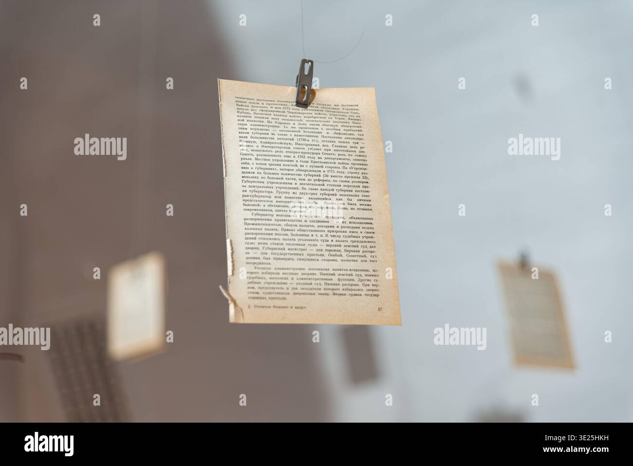 Mosca, Russia - 11 dicembre 2025 - una pagina stampata obsoleta viene sospesa da una linea sottile da una piccola clip di metallo, con altre pagine leggermente sfocate nella Foto Stock