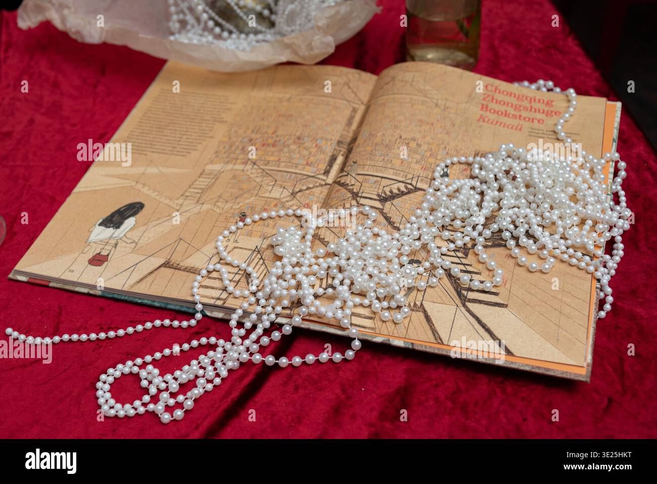 Mosca, Russia - 11 dicembre 2025 - le collane di perle bianche sono drappeggiate e aggrovigliate in un libro illustrato aperto appoggiato su un ricco tessuto di velluto rosso, Foto Stock