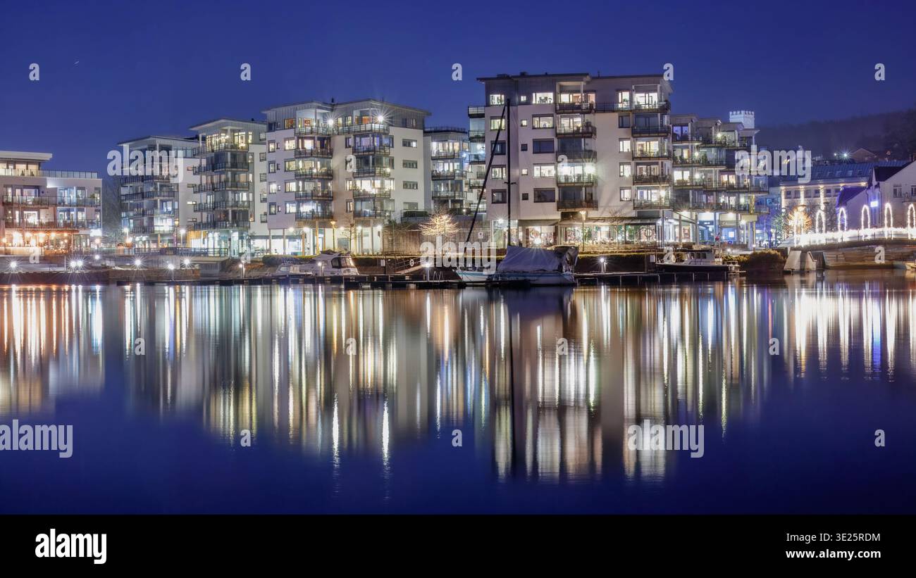 Ora blu, il carattere settentrionale dell'architettura illuminata sul lungomare si riflette nel fiume di notte a Porsgrunn, Norvegia, catturando facciate strutturate e Scand Foto Stock
