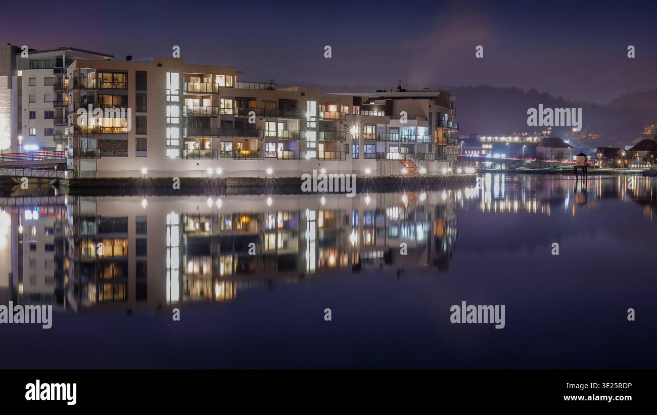 La tradizione vivente del porto nordico ha illuminato i blocchi residenziali lungo il fiume a Porsgrunn, Norvegia, che si riflettono nell'acqua naturale con balconi strutturati e. Foto Stock