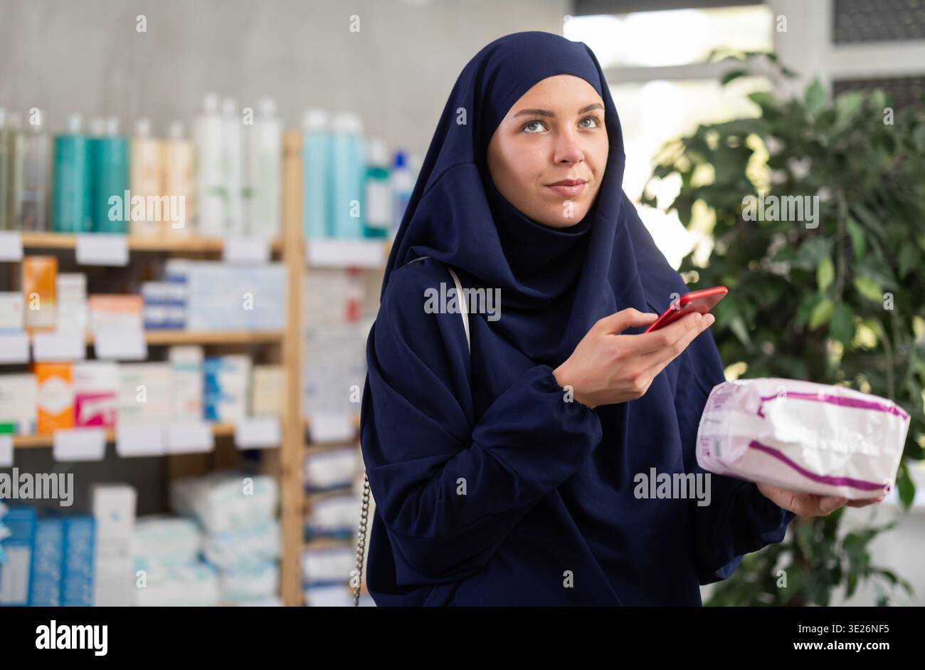 Donna musulmana che effettua la scansione di codici a barre per leggere le recensioni dei pad in farmacia Foto Stock