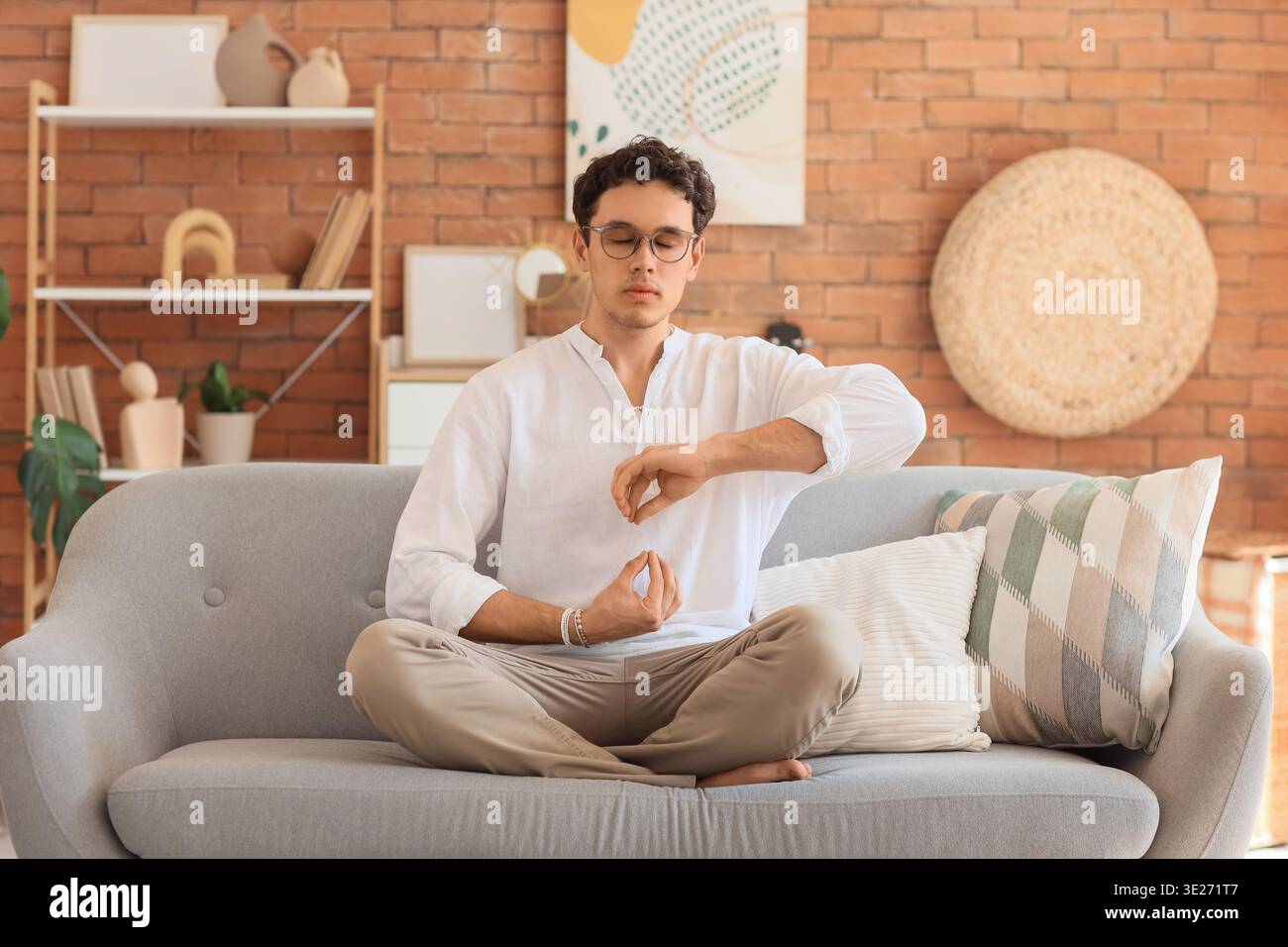 Giovane uomo che medita sul divano a casa Foto Stock