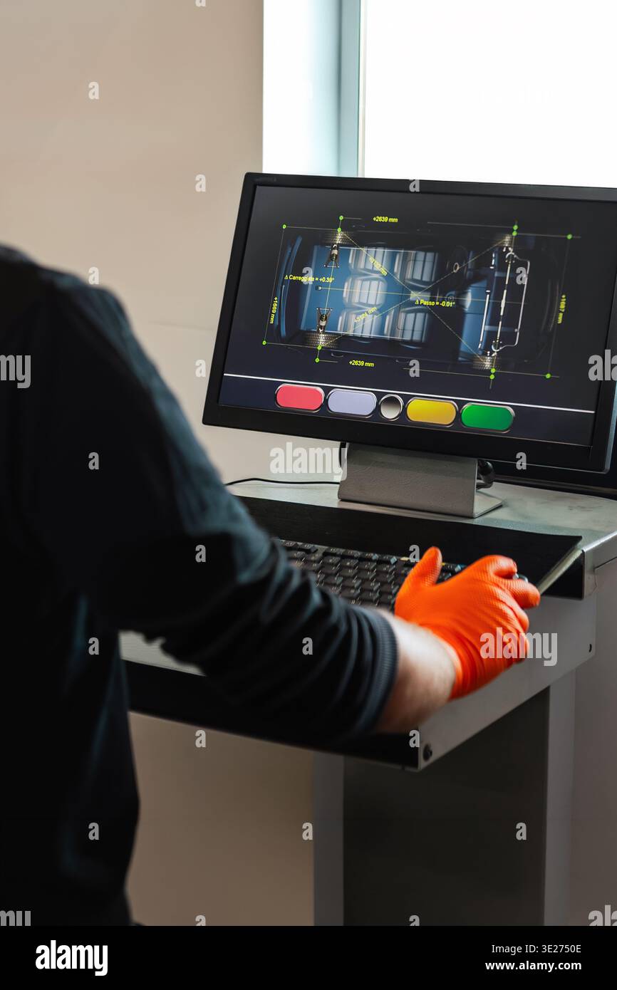 Il meccanico utilizza la tastiera e il monitor per visualizzare il software diagnostico dell'allineamento delle ruote. La schermata mostra la vista del veicolo in alto con misurazioni millimetriche di Foto Stock