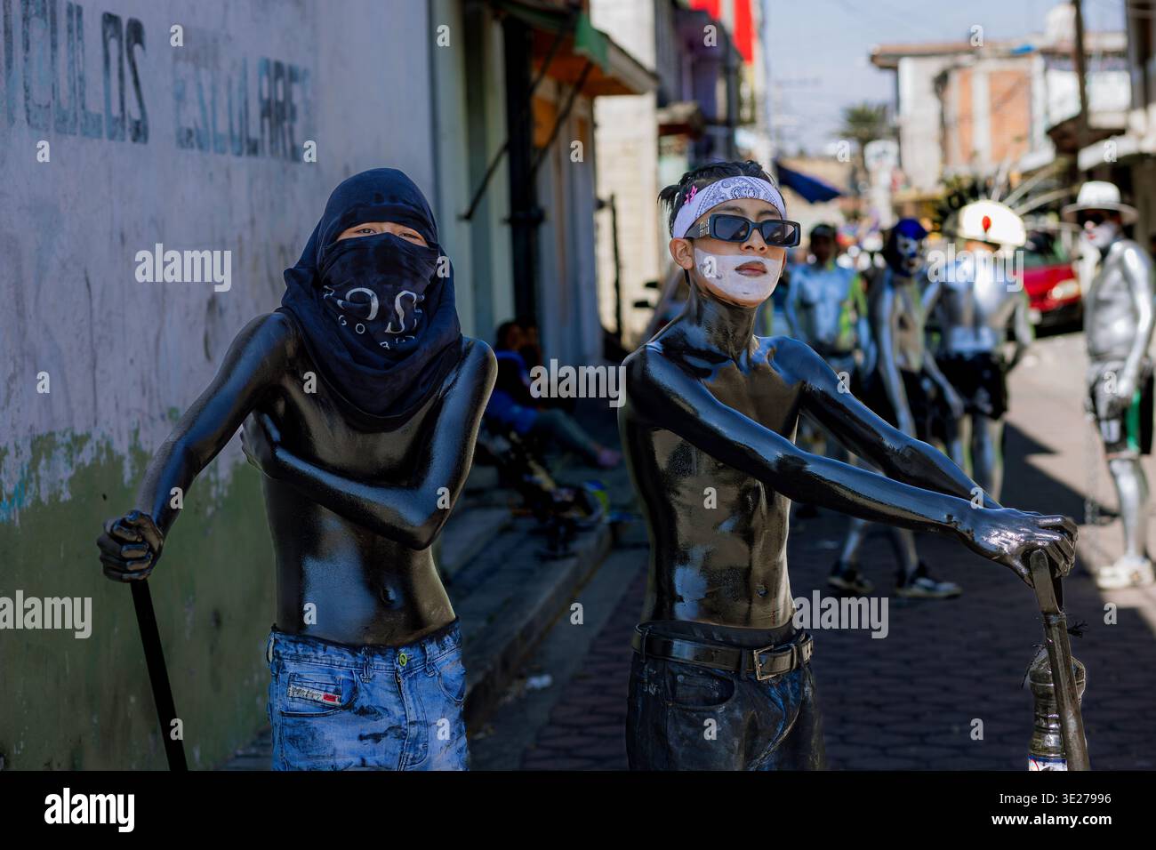 Due giovani partecipanti al carnevale, ricoperti di vernice nera lucida per il corpo con volti ricoperti o fatti Foto Stock