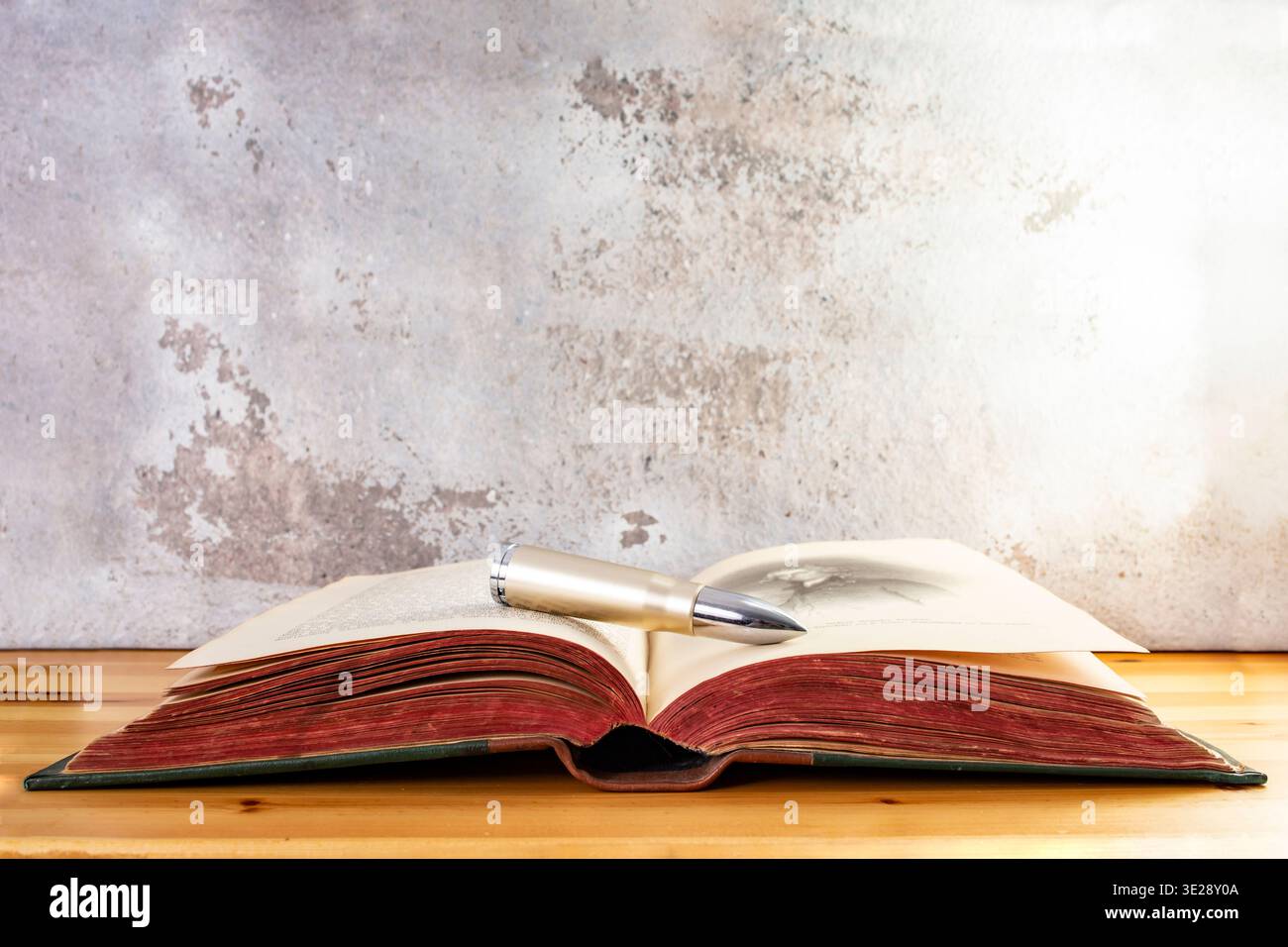 Proiettile su un libro vintage aperto con pagine rosse su una scrivania di legno, omicidi religiosi Foto Stock