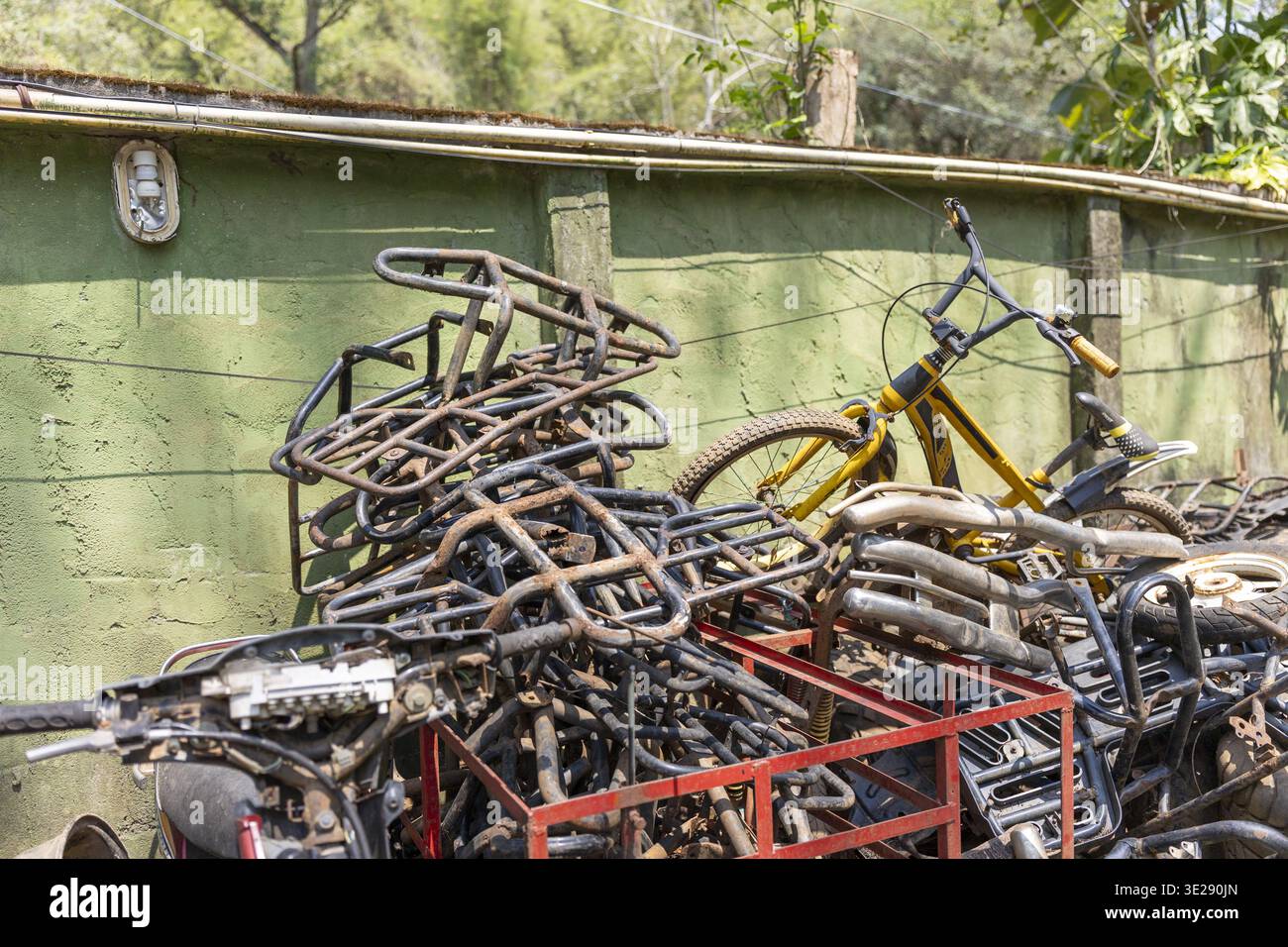 Un mucchio di vecchie parti in metallo arrugginite, tra cui telai per biciclette e componenti per motociclette abbandonate all'aperto accanto al muro verde che evoca Forgotten e nos Foto Stock