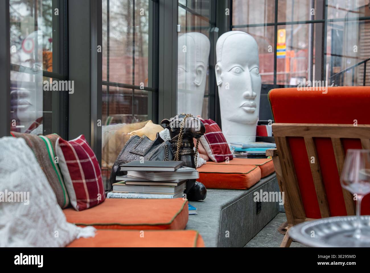 Lounge moderna con panca arancione, sculture bianche della testa e finestre della città Foto Stock
