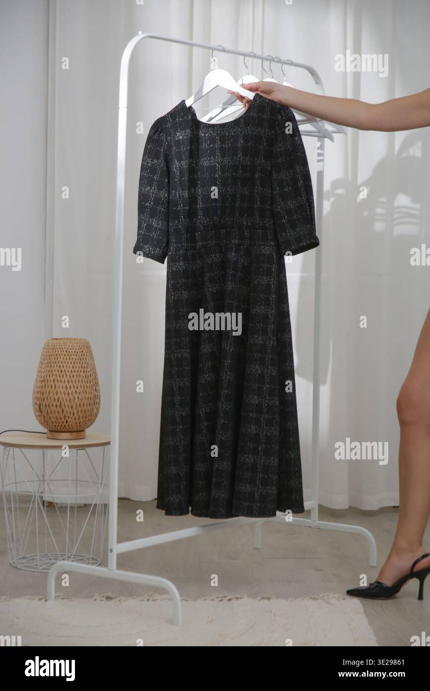 Scena di atelier di moda con un abito longuette nero esposto su un appendiabiti. Ideale per studi di design alla moda, marchi di boutique, prodotti di abbigliamento Foto Stock