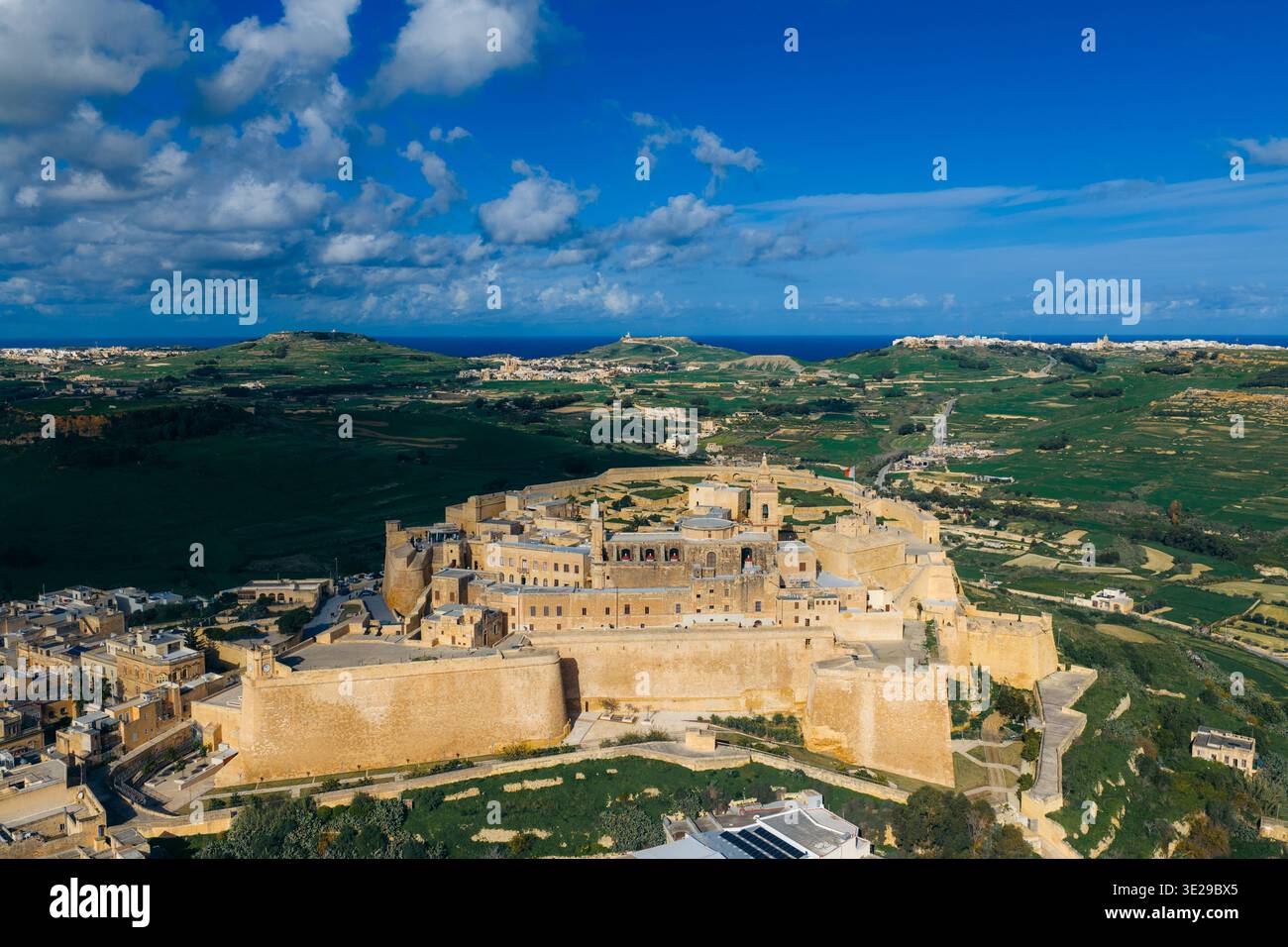 Vista aerea delle pareti di pietra color miele della Cittadella crogiolano al sole, contrastando con il cielo blu profondo e il paesaggio verde circostante, Victor Foto Stock