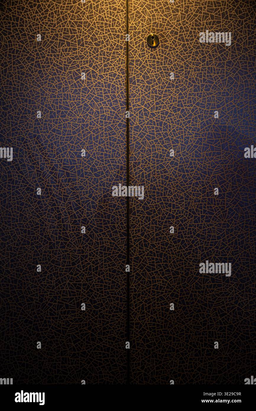 Porta decorata a mosaico d'oro con buco a serratura e stretta cucitura verticale, ingresso astratto illuminato blu Foto Stock
