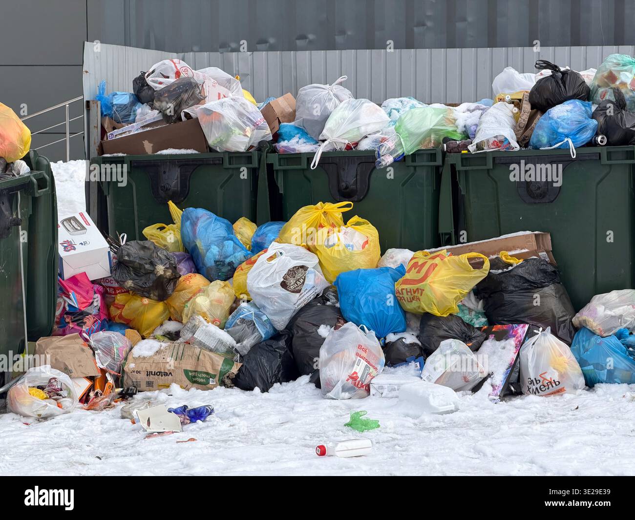 Tambov, Federazione Russa - 25 febbraio 2026 bidoni della spazzatura verdi e pile di sacchi per rifiuti domestici sulla neve in una zona residenziale - Immagine stock catturata con smartphone