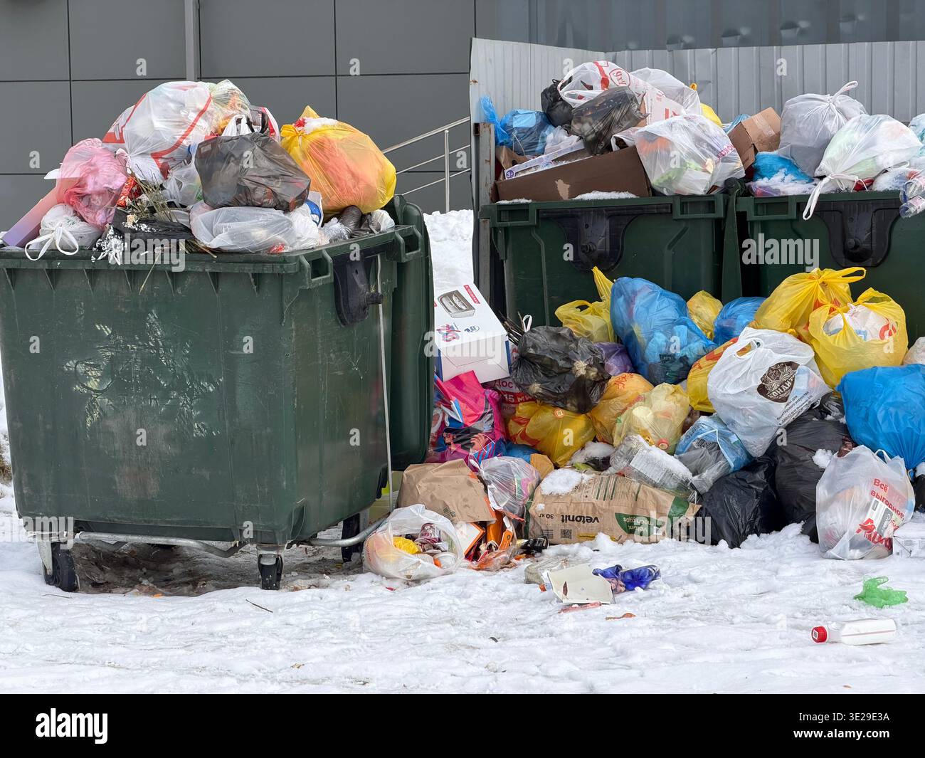 Tambov, Federazione Russa - 25 febbraio 2026 bidoni della spazzatura verdi e pile di sacchi per rifiuti domestici sulla neve in una zona residenziale durin - Immagine stock catturata con smartphone