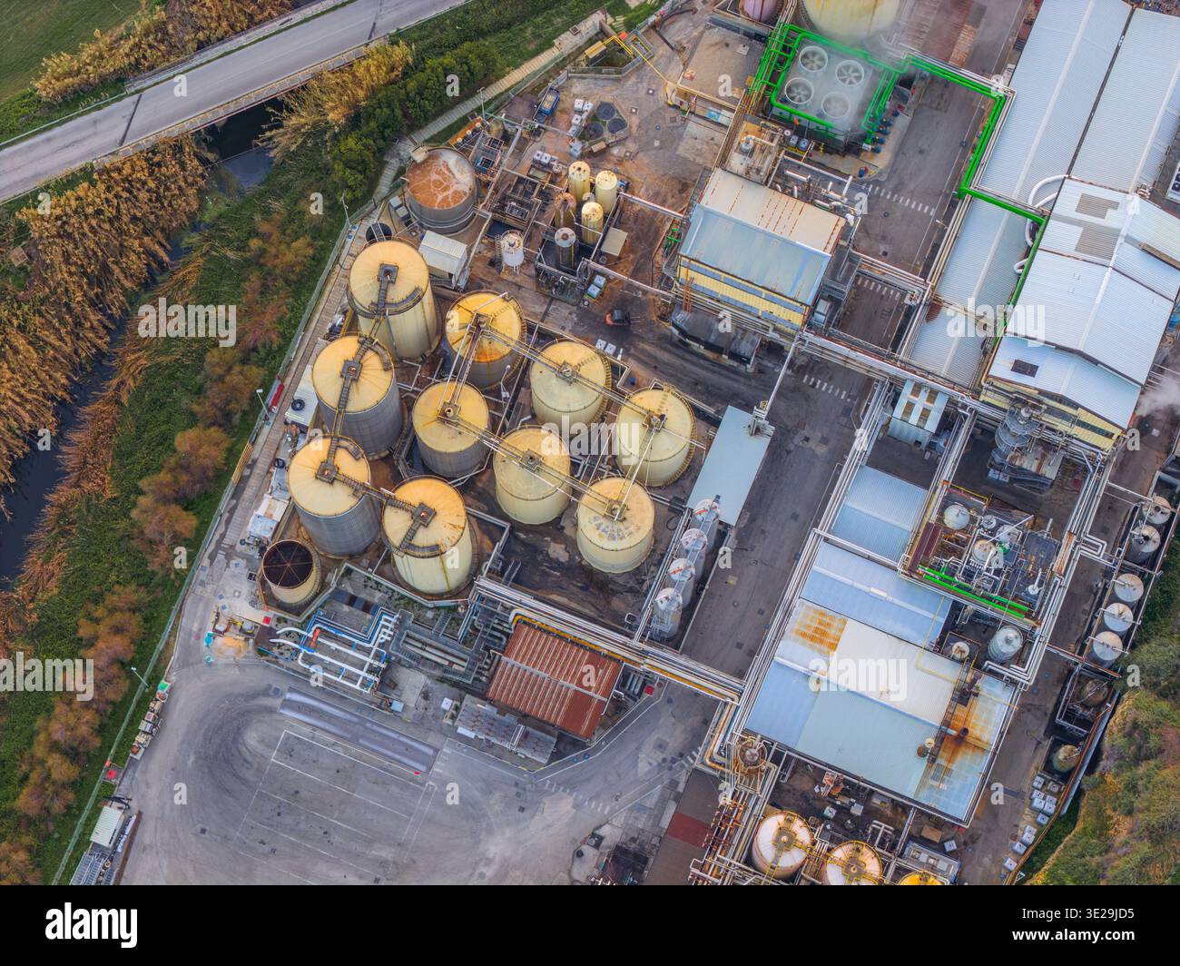 Veduta aerea di un paesaggio industriale in cui le cisterne metalliche si raggruppano, riflettendo il cielo morbido sopra, in mezzo a una rete di tubi e strutture, vasto, A. Foto Stock