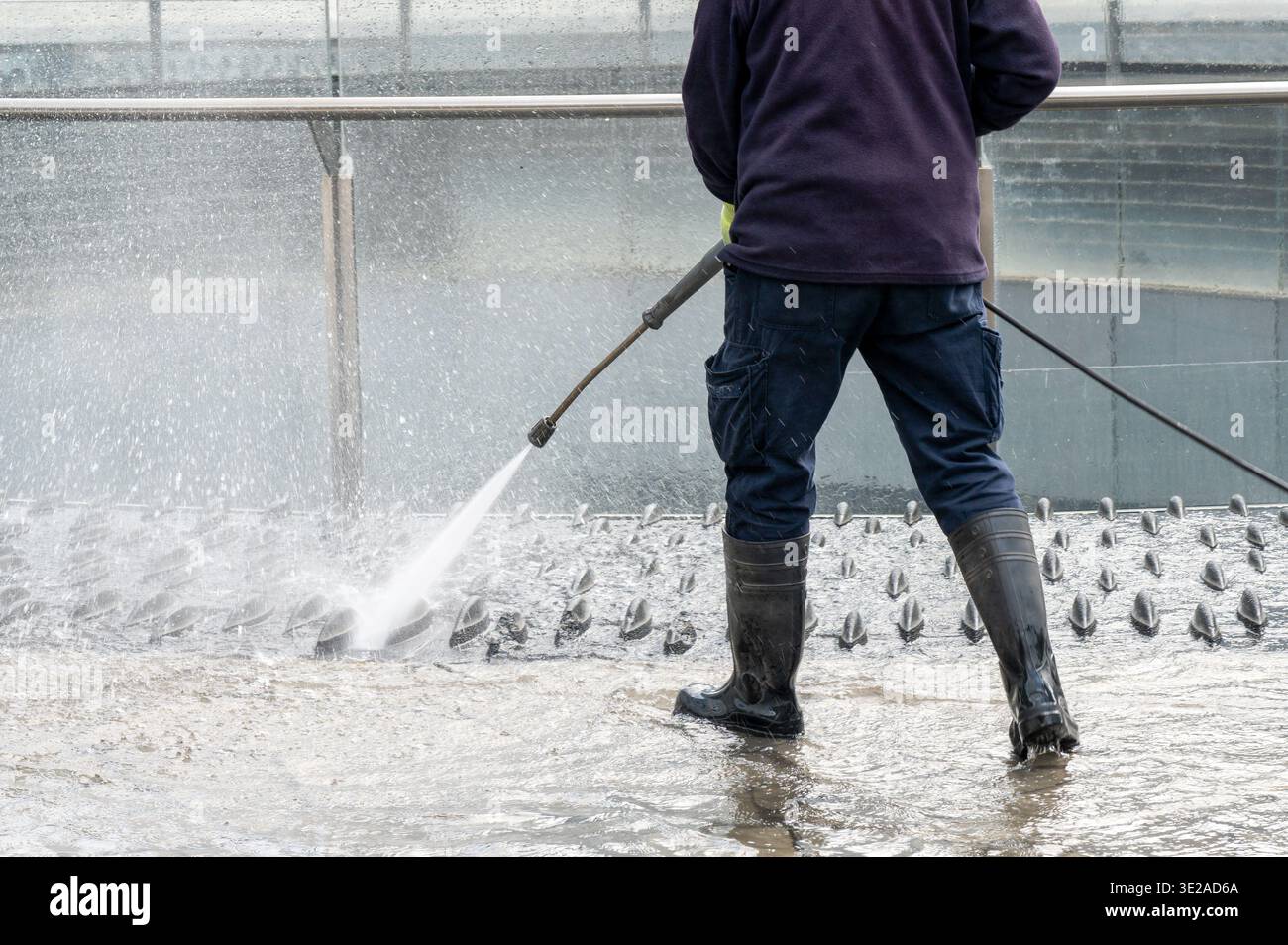 Persona che spruzza un forte flusso d'acqua per pulire il pavimento in cemento e le strutture metalliche Foto Stock