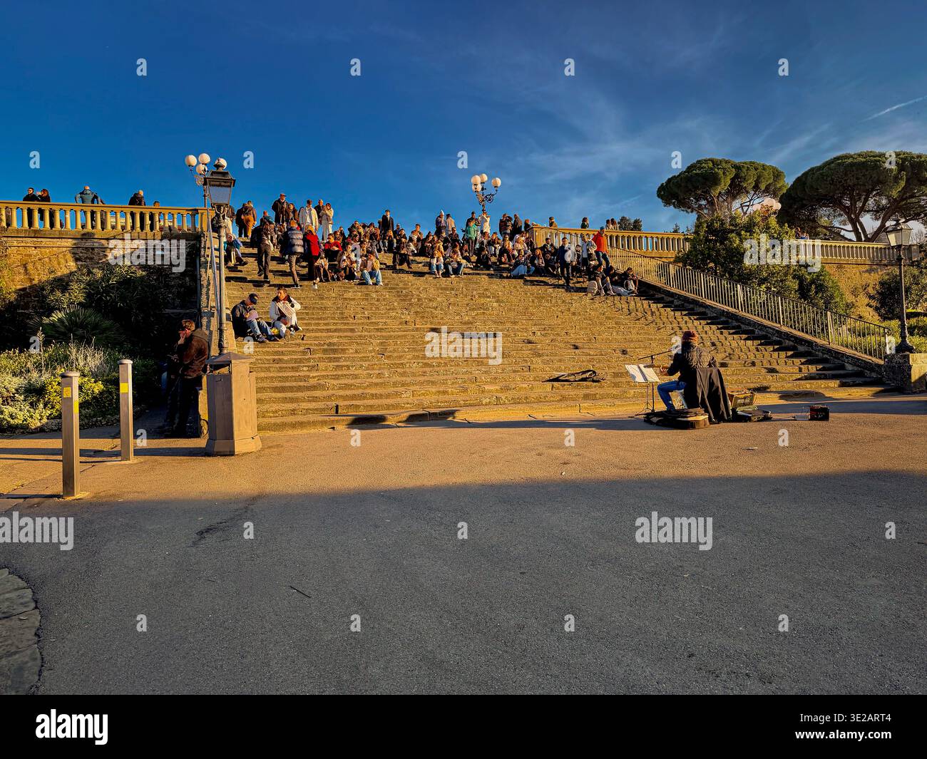 Persone sedute sui gradini ascoltando un intrattenitore di strada a Piazzale Michelangelo, un famoso punto panoramico collinare a Firenze, in Italia Foto Stock