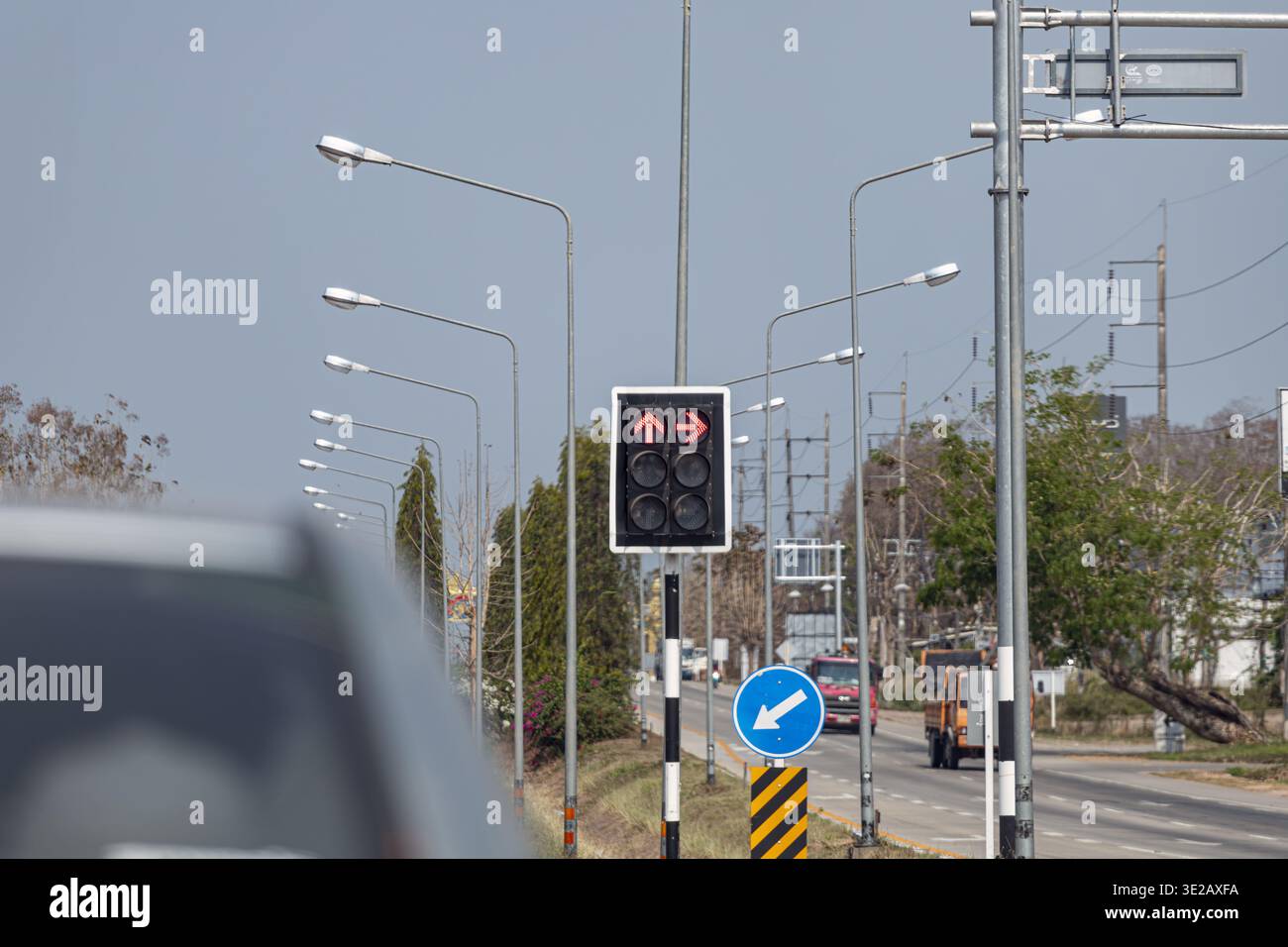 Un semaforo con freccia rossa che mostra i segnali di stop in un incrocio stradale urbano in Thailandia, circondato da file di lampioni, una direzione blu Foto Stock