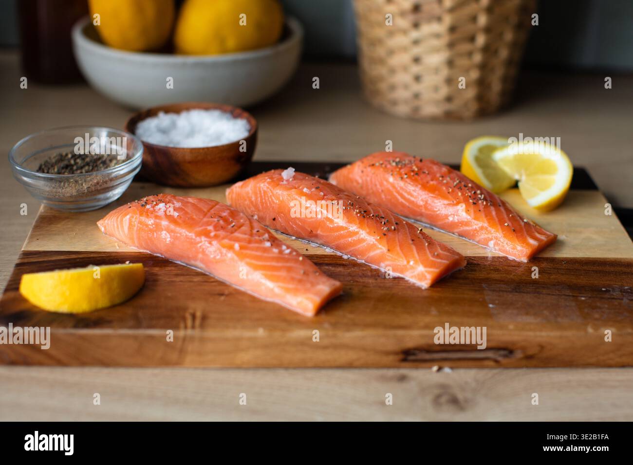 filetti di salmone conditi con cristalli di sale marino e pepe nero screpolato, disposti su un tagliere in legno bicolore con spicchi di limone. Foto Stock