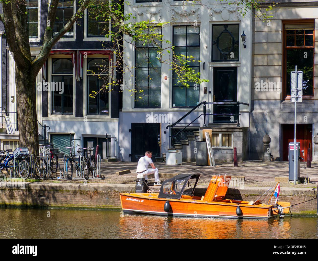 Un'affascinante barca in legno ormeggiata su un tranquillo canale di Amsterdam, Olanda, circondata da storici edifici in mattoni. Foto Stock