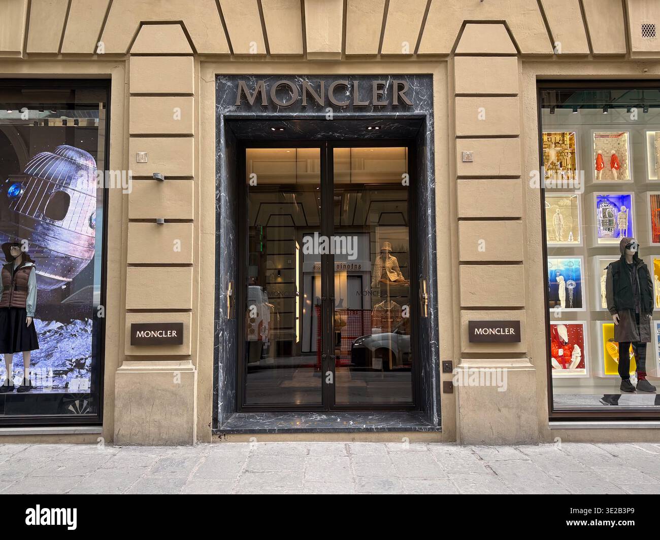 Moncler. Firenze, Italia. L'ingresso di lusso del marchio di outerwear è incorniciato da un'architettura classica in pietra. Pavimentazione stradale vuota. Foto Stock