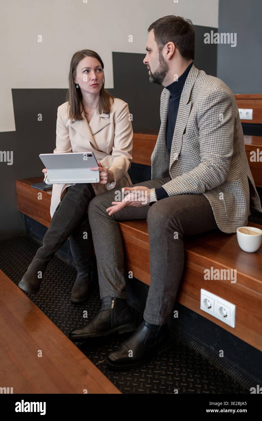 Uomo e donna che esaminano le informazioni sul tablet alla scrivania di legno durante la pausa caffè in ufficio. Revisione tablet, pausa caffè, affari, informazioni Foto Stock