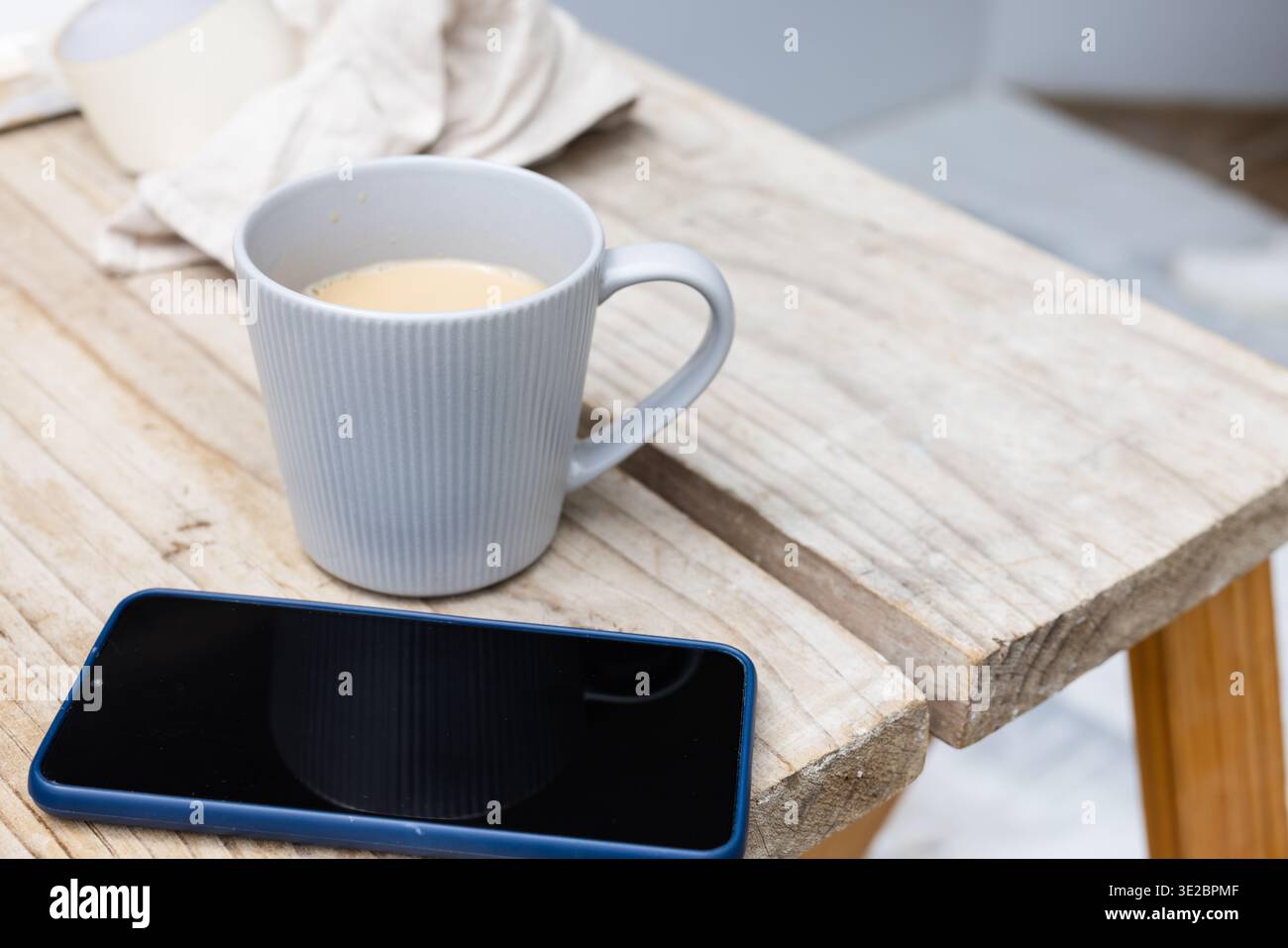 Mostra la tazza in ceramica grigio chiaro seduta sul tavolino a schiera, con smartphone con rivestimento blu. Woodgrain, rustico, latte, dispositivo, gadget, calma, mini Foto Stock