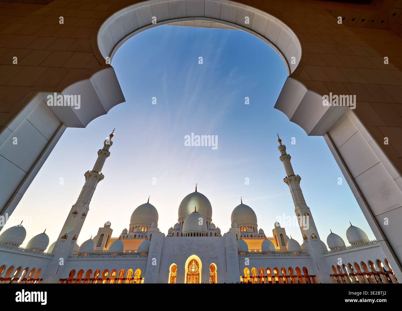Il tramonto rivela la silhouette della grande Moschea dello sceicco Zayed ad Abu Dhabi. I visitatori esplorano lo spazio mentre le luci iniziano a brillare. Foto Stock