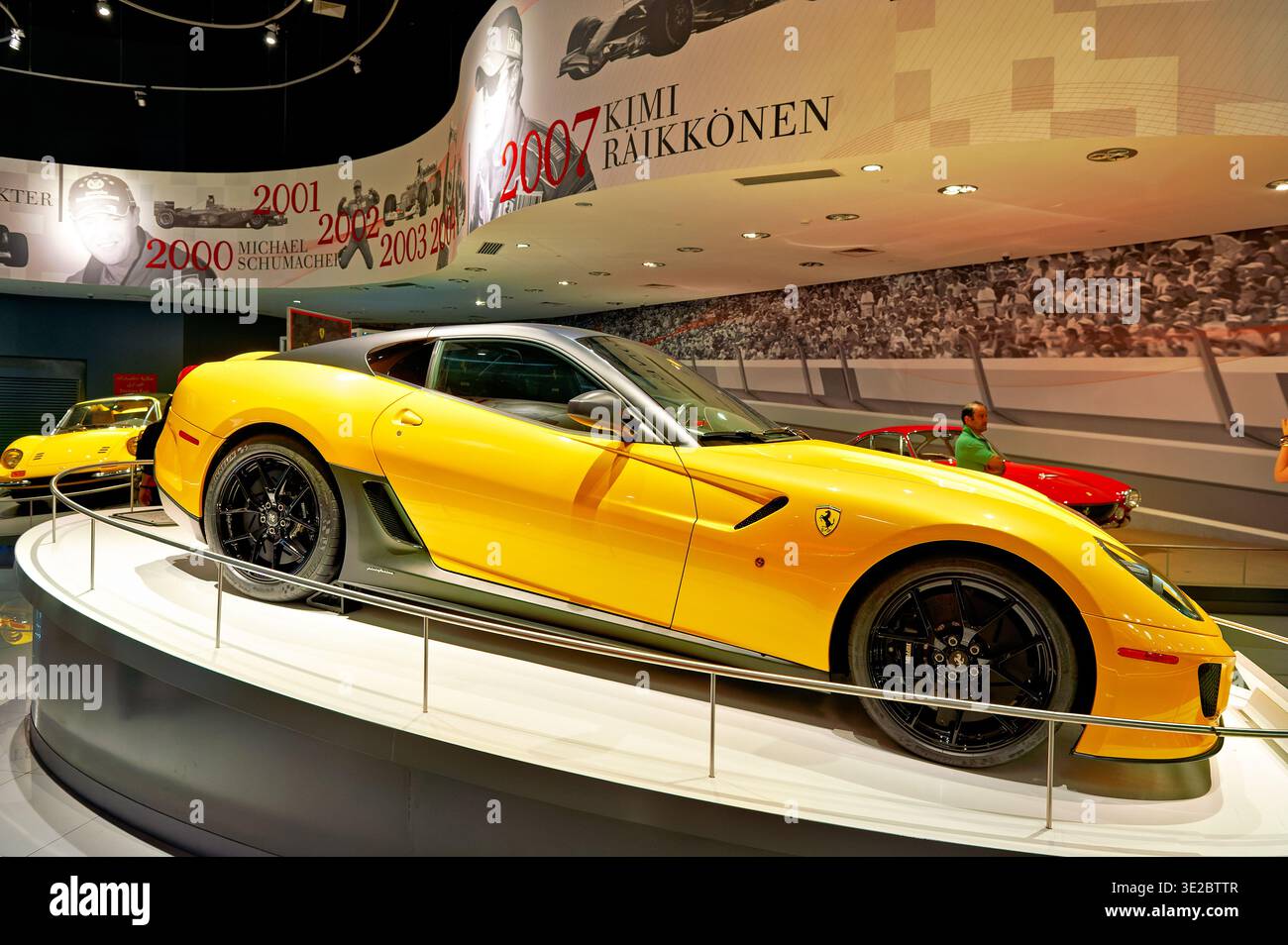 I visitatori ammirano una Ferrari gialla nel Ferrari World di Abu Dhabi. L'attrazione mostra le auto famose e la loro storia. Foto Stock